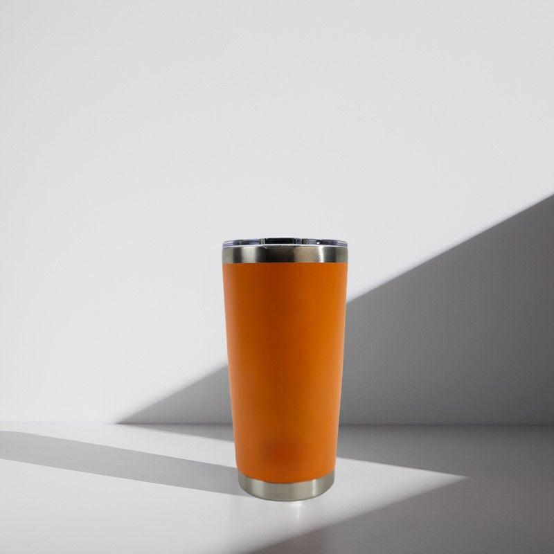 Orange tumbler with silver base and rim on a light gray background