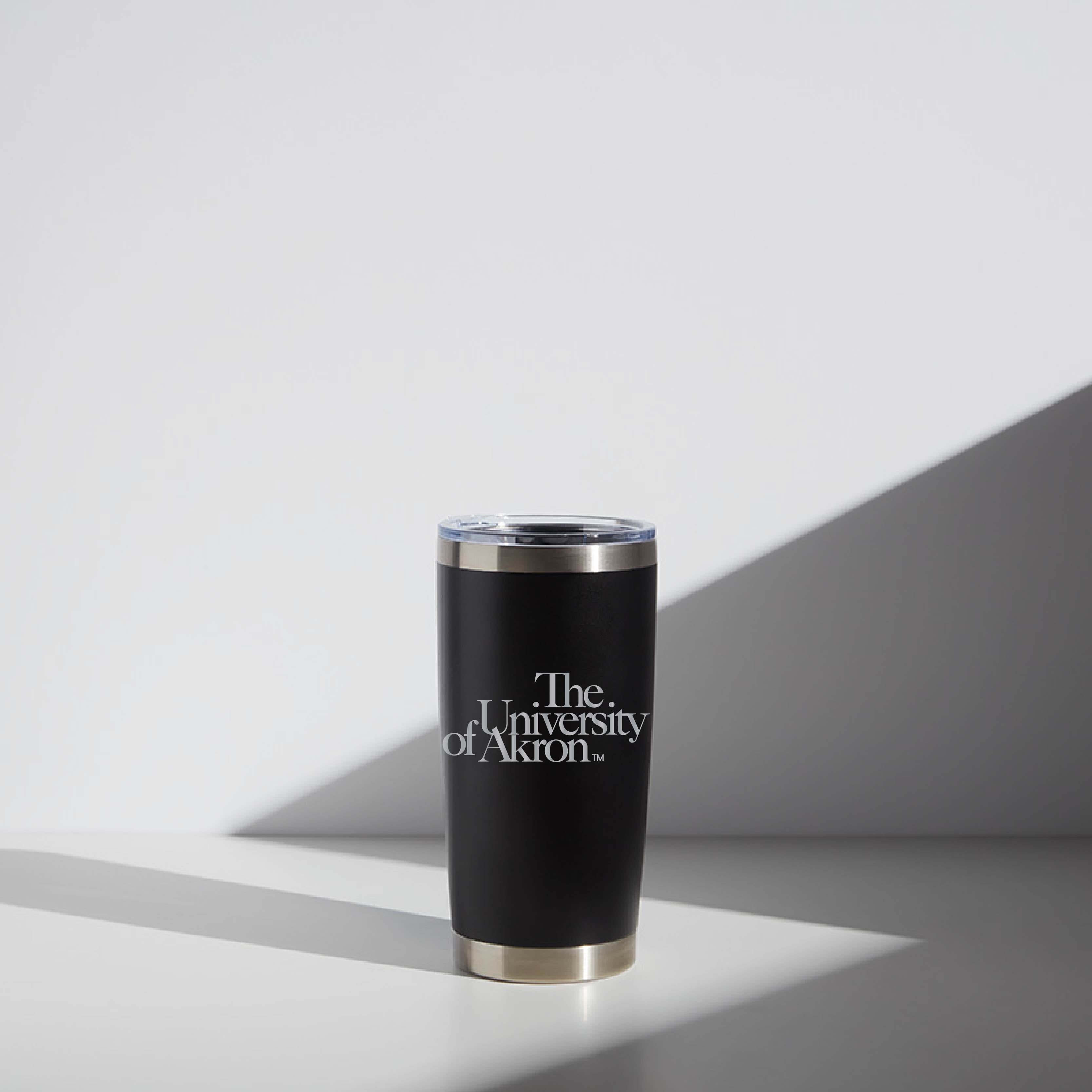 Black 20 oz WATR Tumbler with "The University of Akron" logo, featuring a silver rim and clear lid, displayed in a well-lit environment with shadow accents.