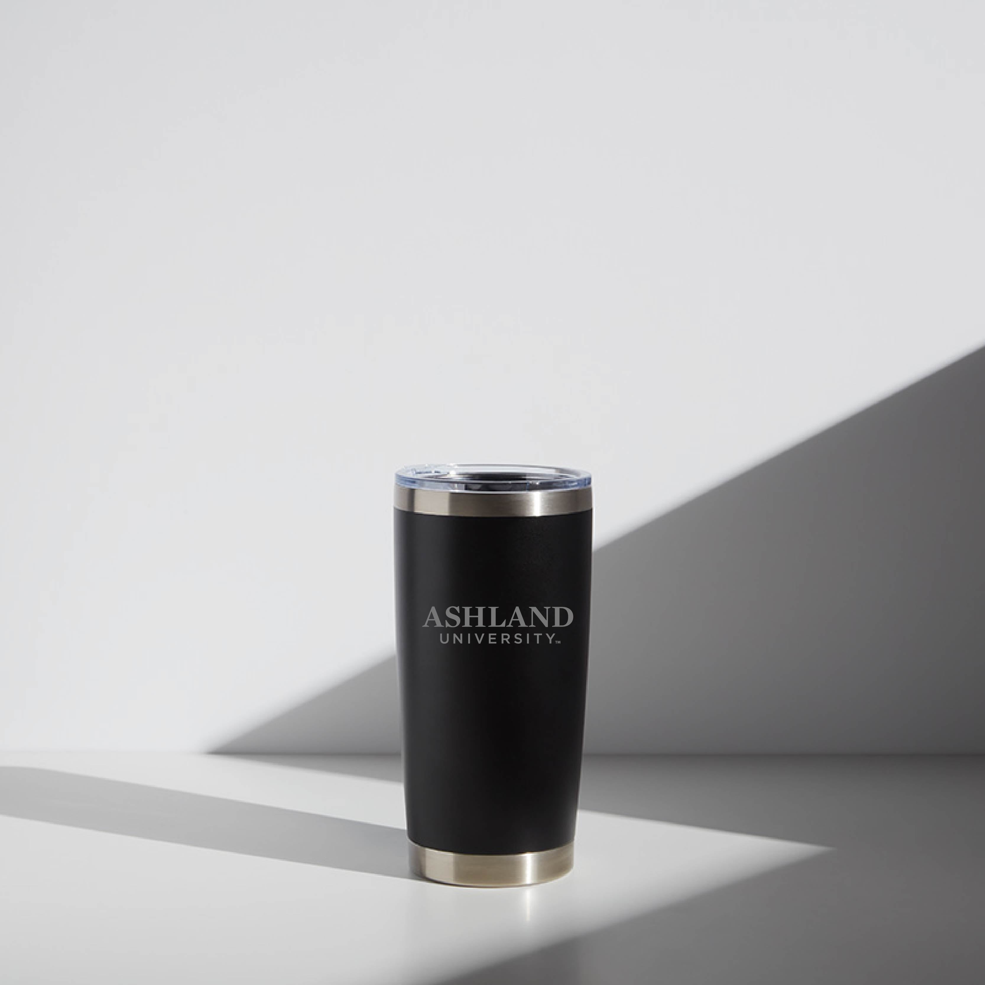 20 oz WATR Tumbler Ashland from Ashland University, featuring a sleek black design with university logo, clear lid, and stainless steel accent at the base, displayed in a bright, minimalist setting.