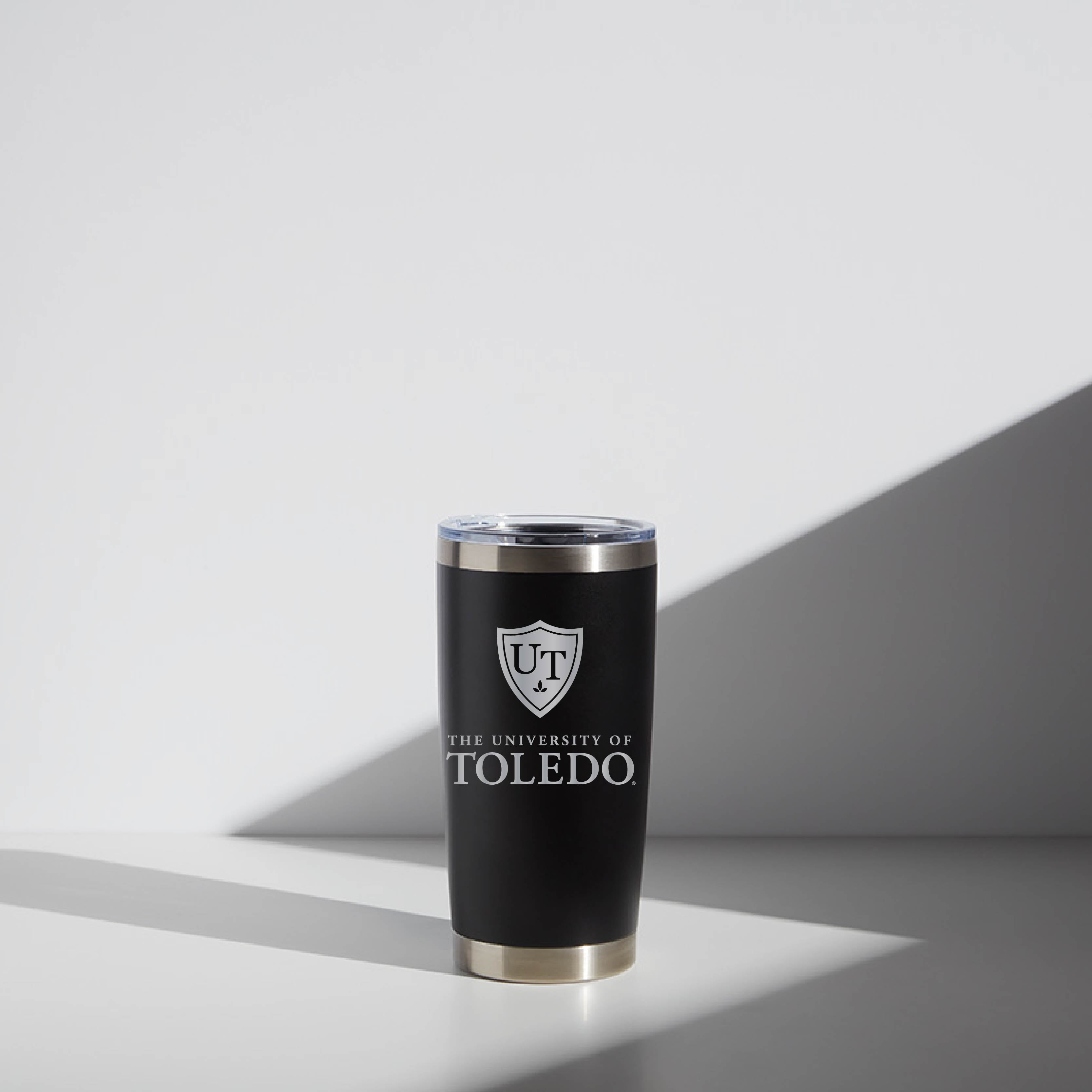 Alt text: "20 oz WATR black tumbler with University of Toledo logo, featuring a clear lid, displayed on a light grey background with slight shadowing."