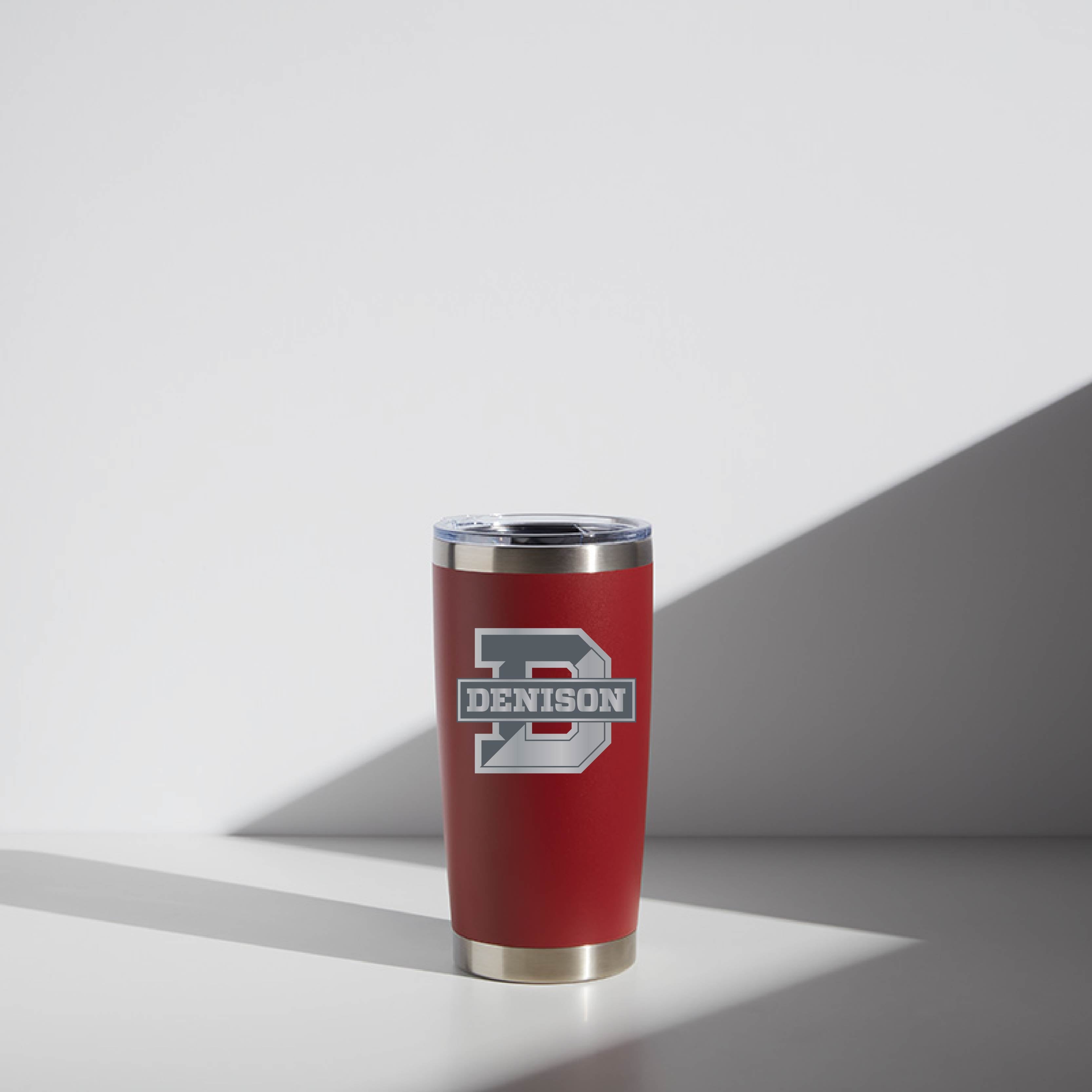 Red 20 oz WATR Tumbler with Denison University logo, featuring a stainless steel rim and clear lid, illuminated by natural light on a simple background.