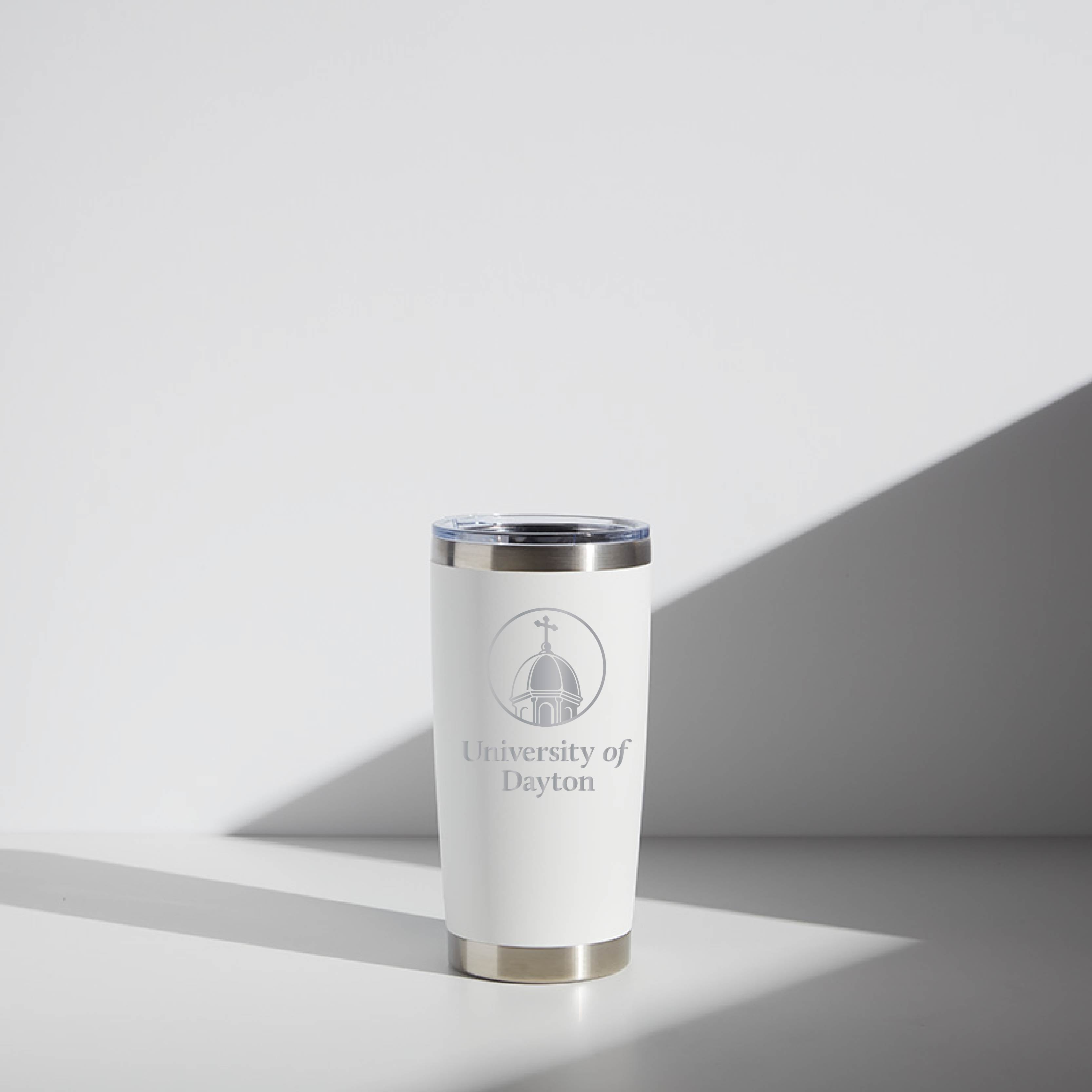 Alt text: "20 oz WATR Tumbler with University of Dayton Chapel logo on a white and silver cup, positioned against a shadowed off-white background."