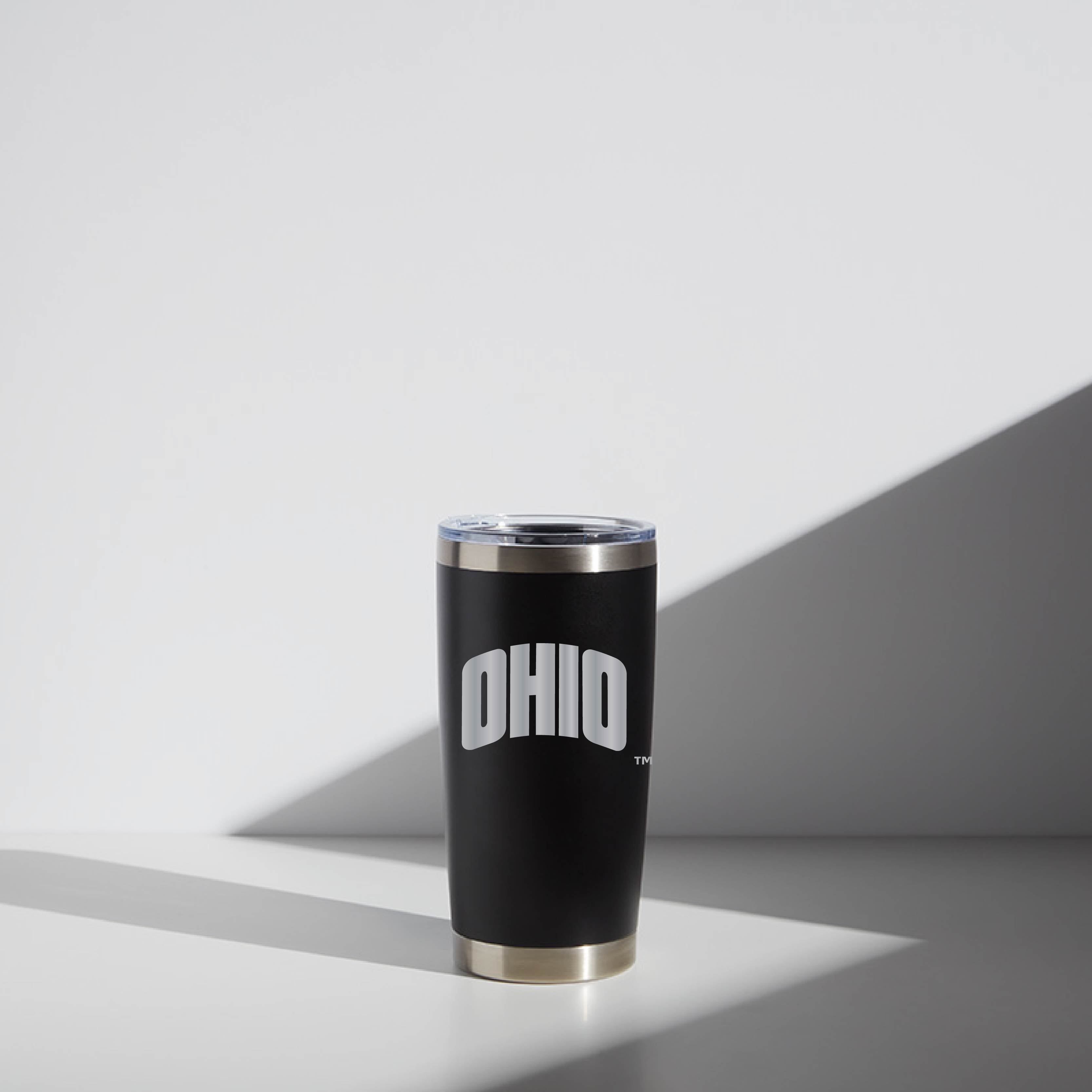 Black 20 oz WATR tumbler with the word "OHIO" printed in large white letters, featuring a stainless steel rim and clear lid, displayed under soft lighting with cast shadows.