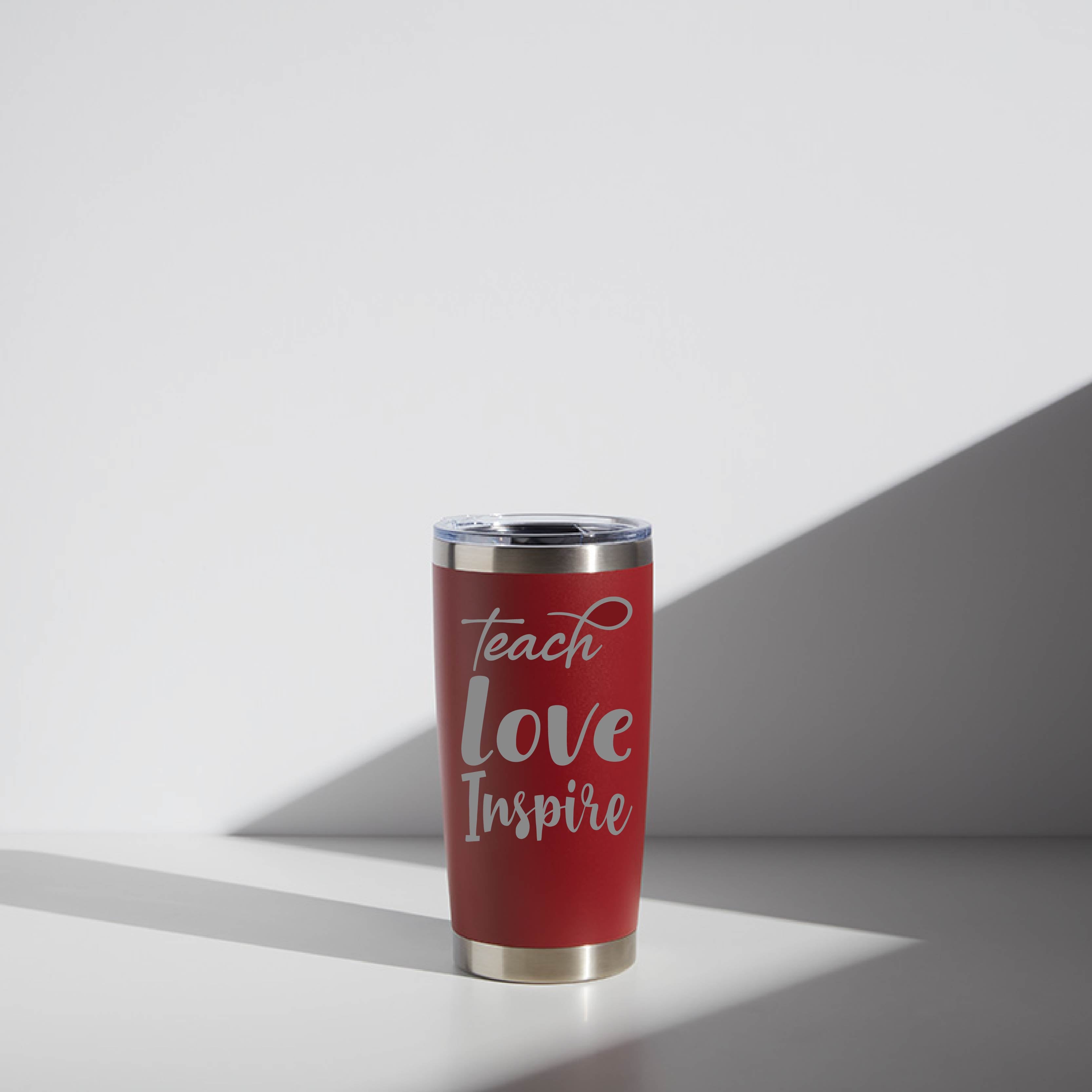Red 20 oz stainless steel tumbler with "Teach Love Inspire" inscription in white script, ideal for teacher gifts, sitting in soft lighting.