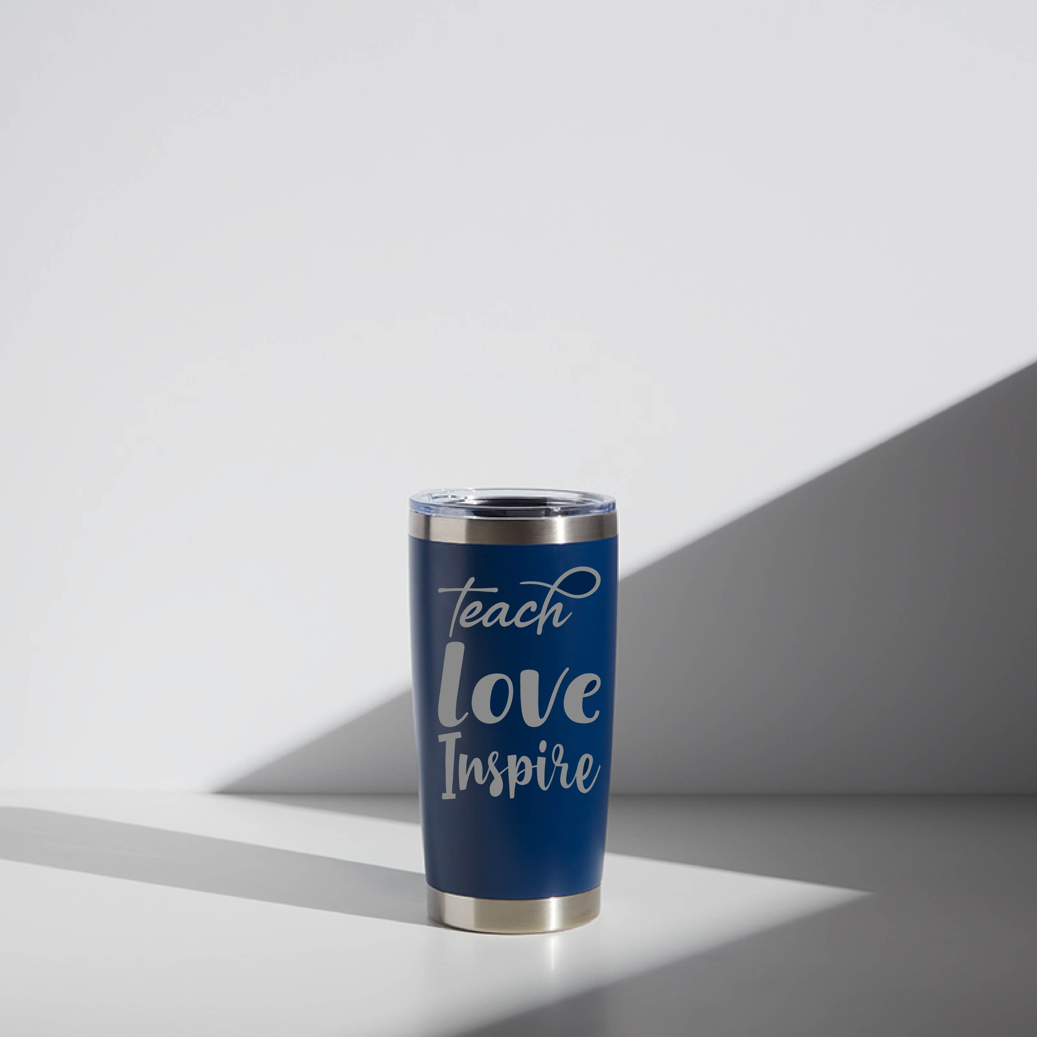 Alt text: "Personalized 20 oz stainless steel tumbler for teachers, featuring a deep blue design with 'Teach Love Inspire' in stylish white font, placed on a light surface with subtle shadows."
