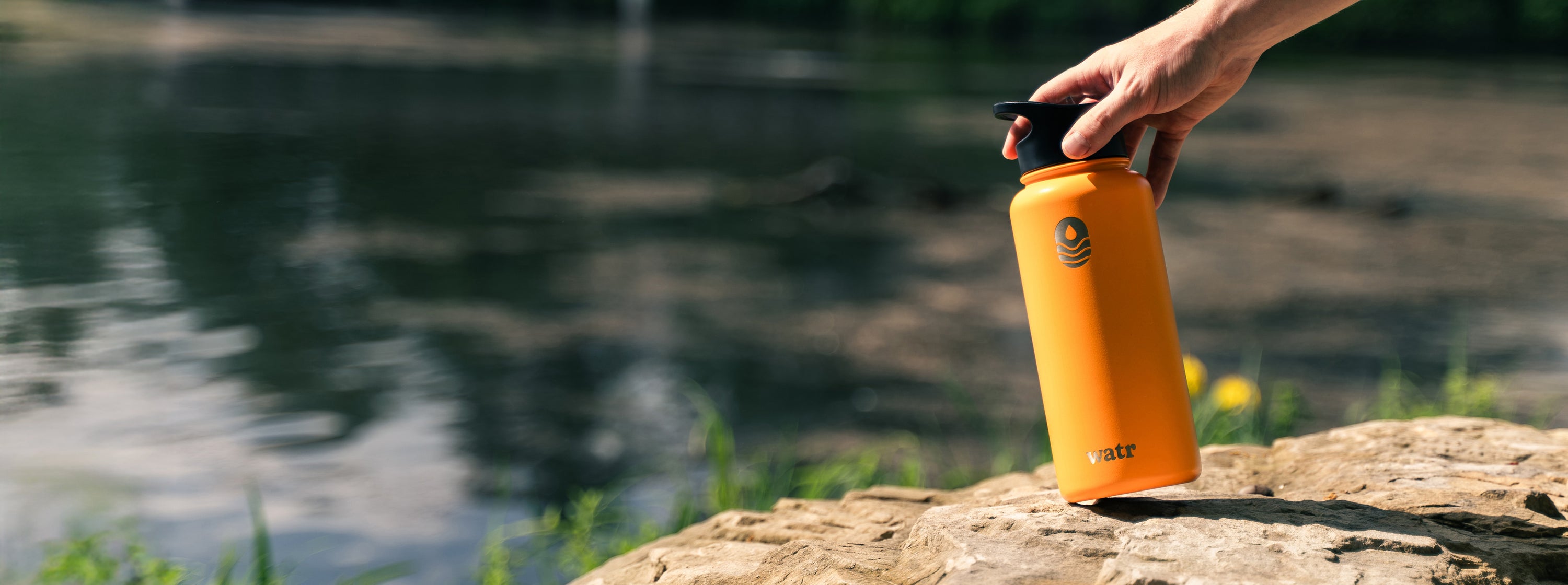 We Are The Ripple Custom Stainless Steel Water Bottle in Orange by a river