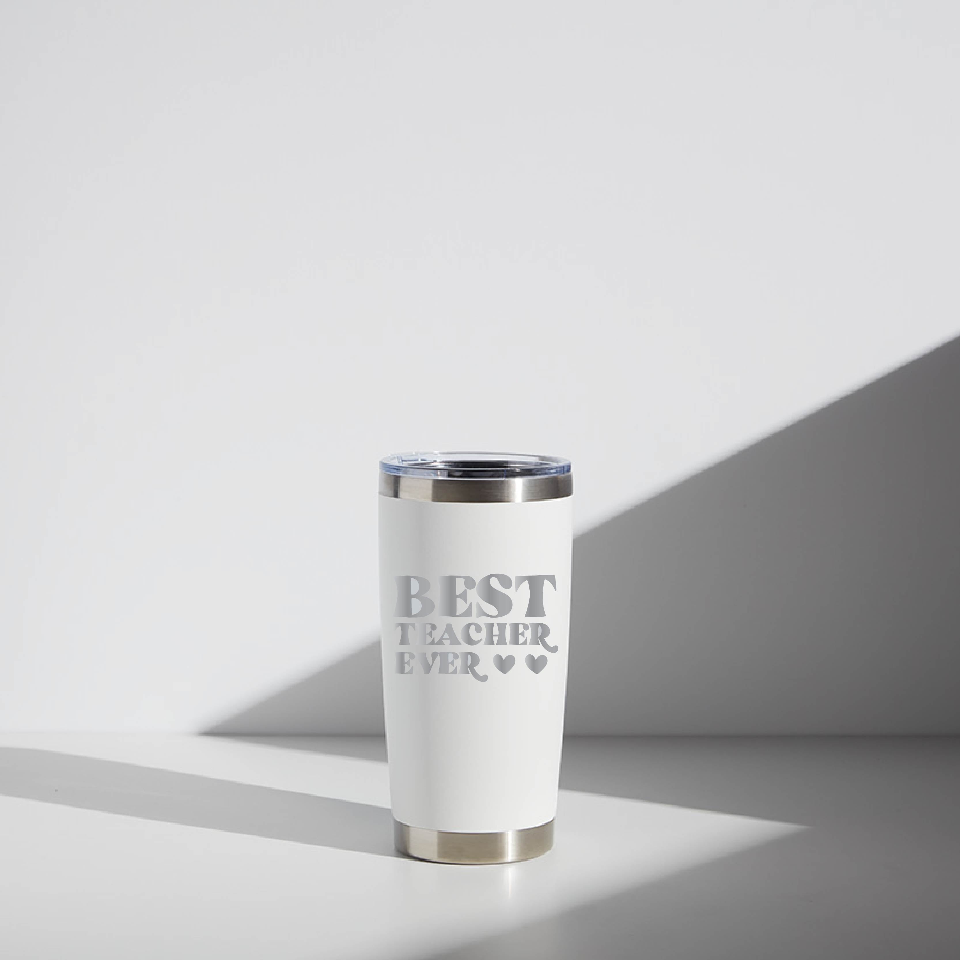 Alt text: "20 oz stainless steel tumbler personalized with 'Best Teacher Ever' text in gray on a white background, placed on a light surface with shadows cast to the side, designed as a teacher gift."