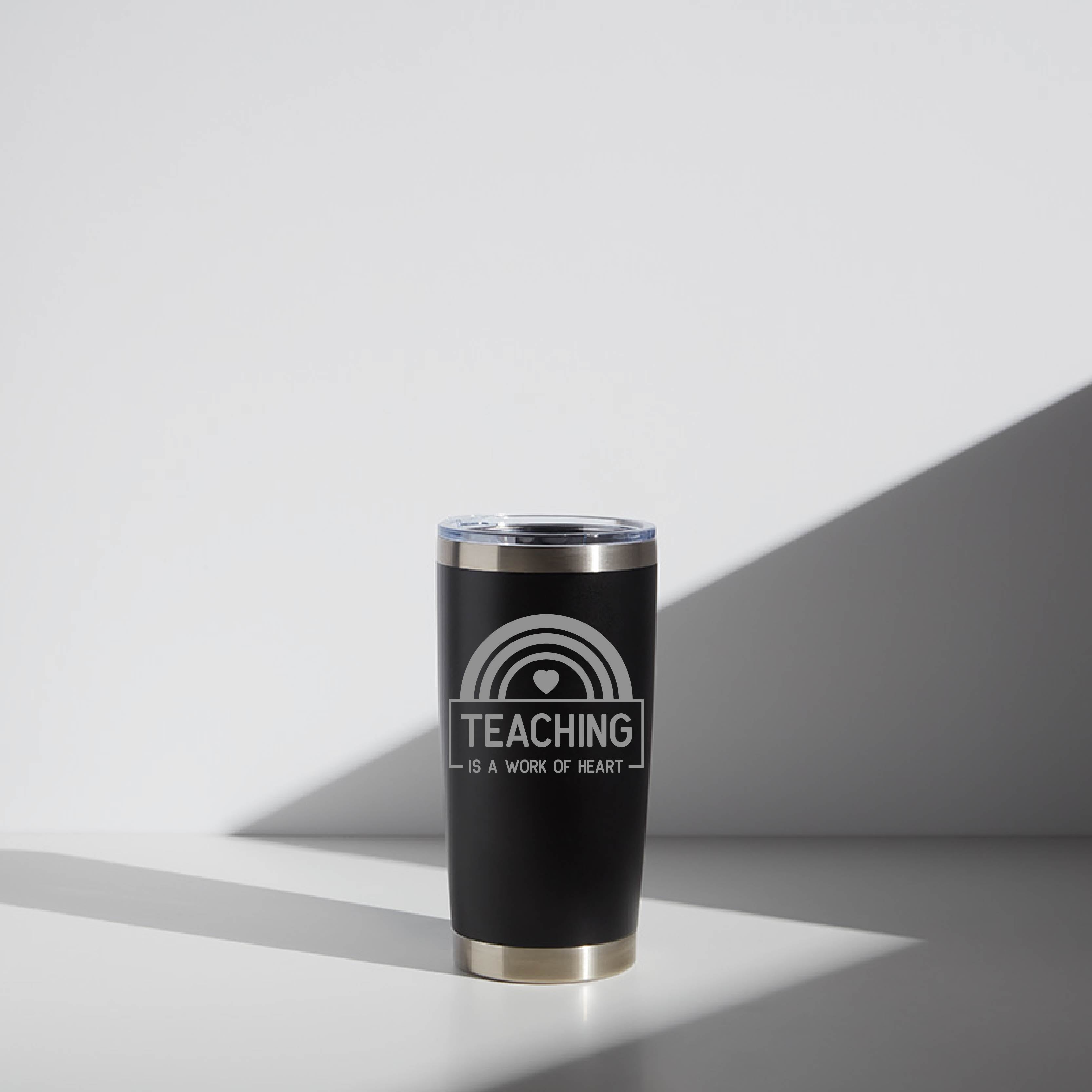 Black 20 oz stainless steel tumbler with clear lid, personalized for teachers with the message "Teaching is a work of heart" printed in white.