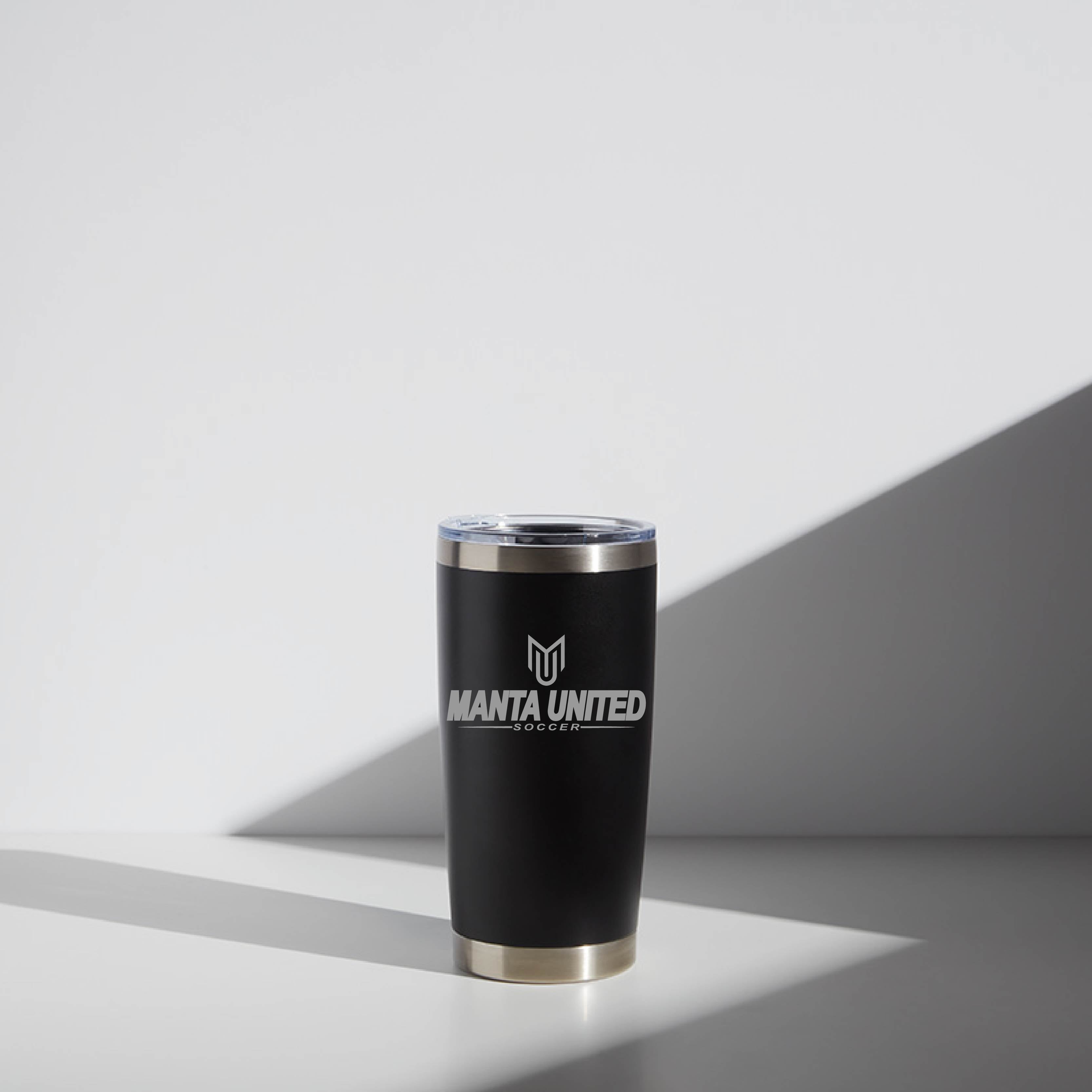 Black 20 oz WATR Tumbler with Manta United Soccer logo, featuring a stainless steel rim and transparent lid, positioned against a minimalist background with geometric shadows.