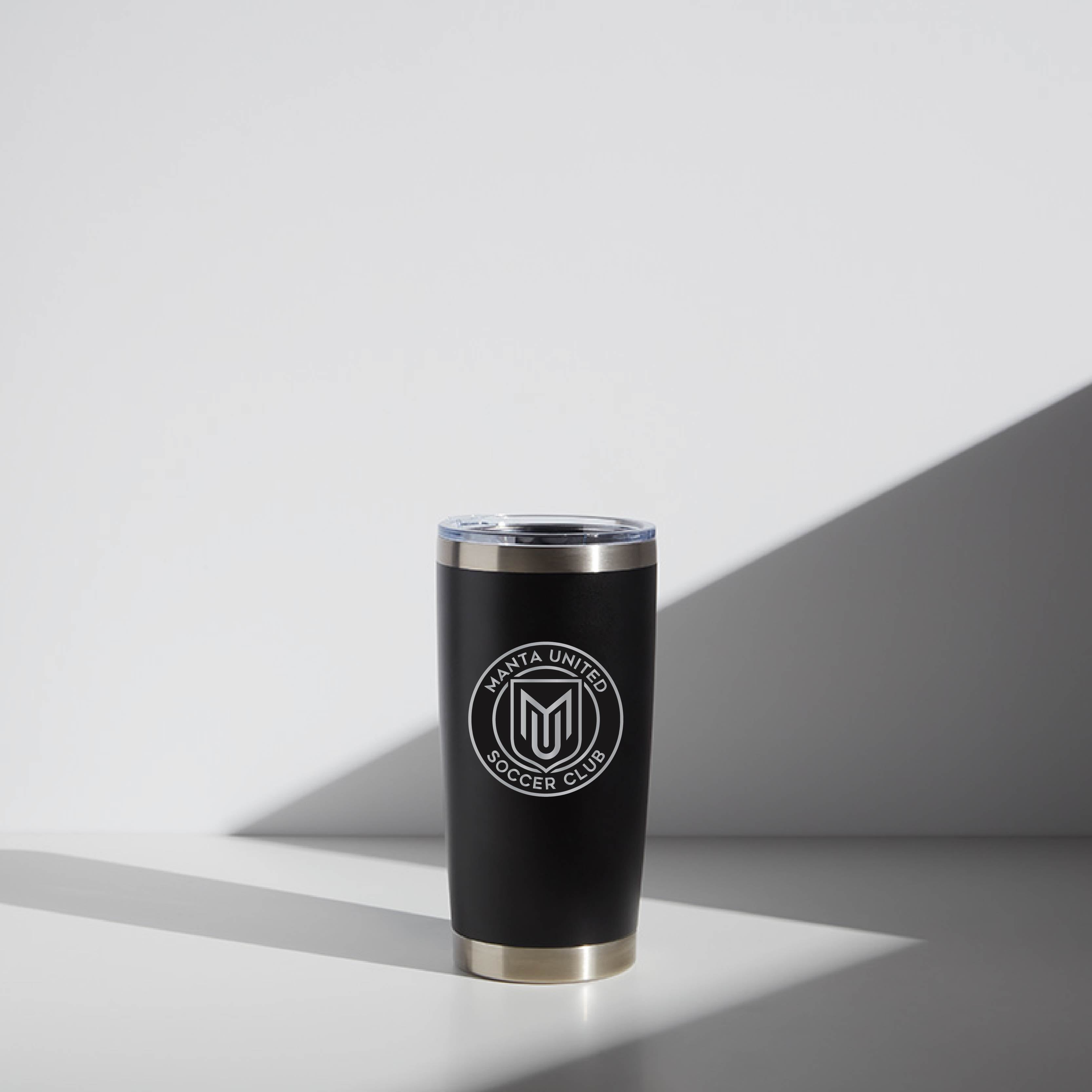 Alt text: "20 oz black WATR tumbler with Manta United Soccer Club logo, featuring a modern design with a silver rim and clear lid, positioned against a light background with a shadow effect."