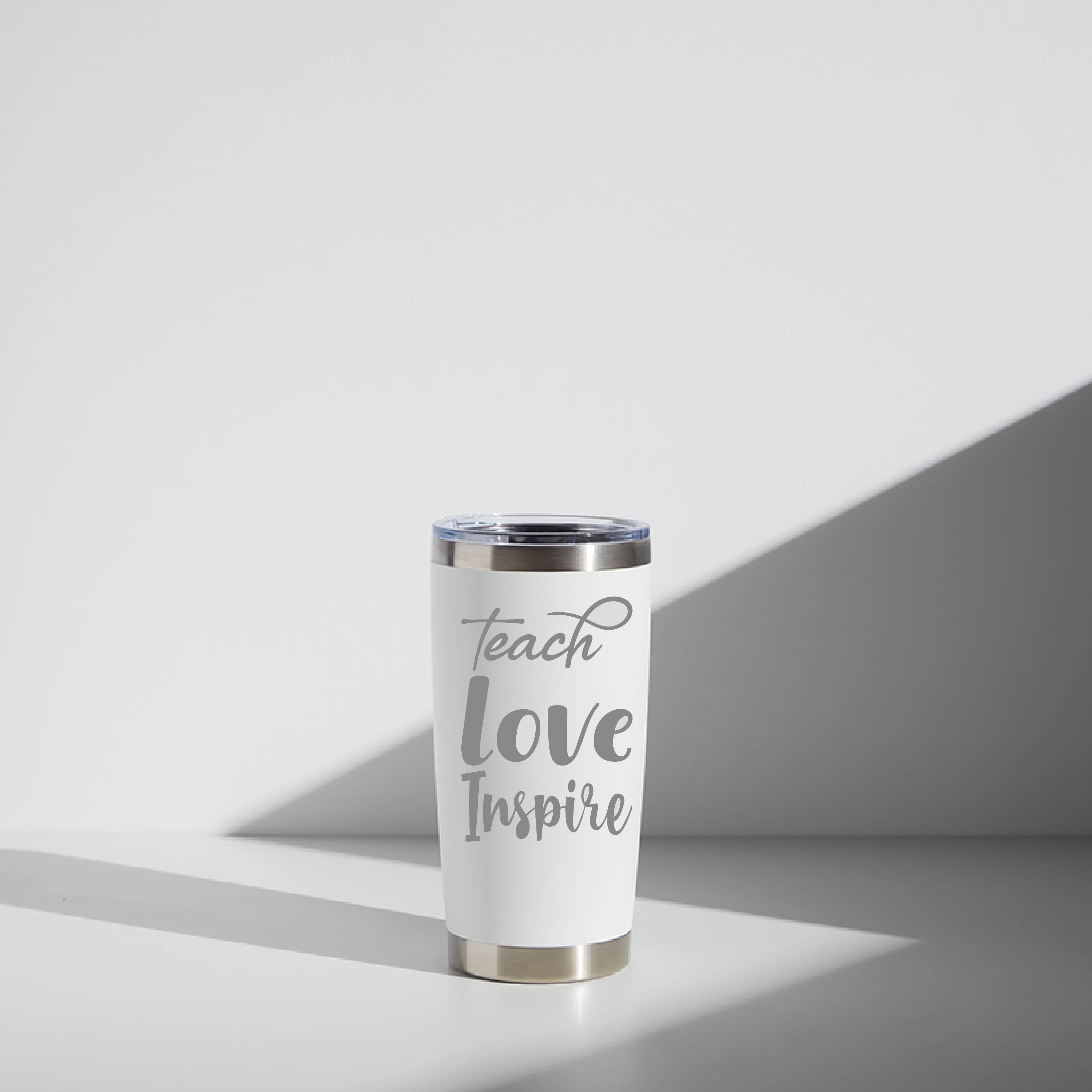 20 oz stainless steel tumbler with the inspirational phrase "Teach Love Inspire" printed in gray on a white background, ideal for personalized teacher gifts, displayed in natural light.