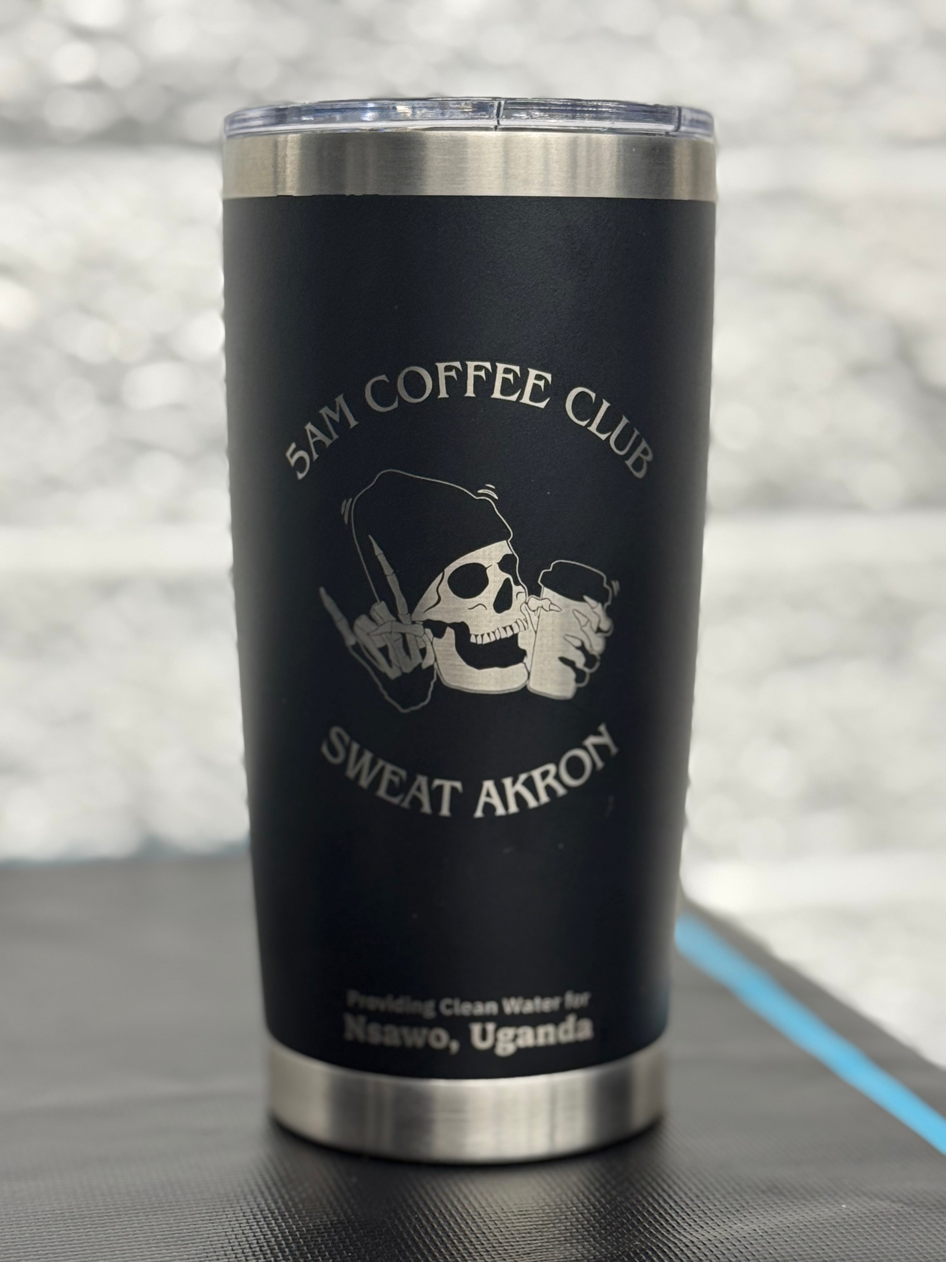 Alt text: "20 oz stainless steel tumbler with black matte finish featuring '5AM Coffee Club' and skull design for SWEAT Akron, promoting clean water for Nsawo, Uganda."