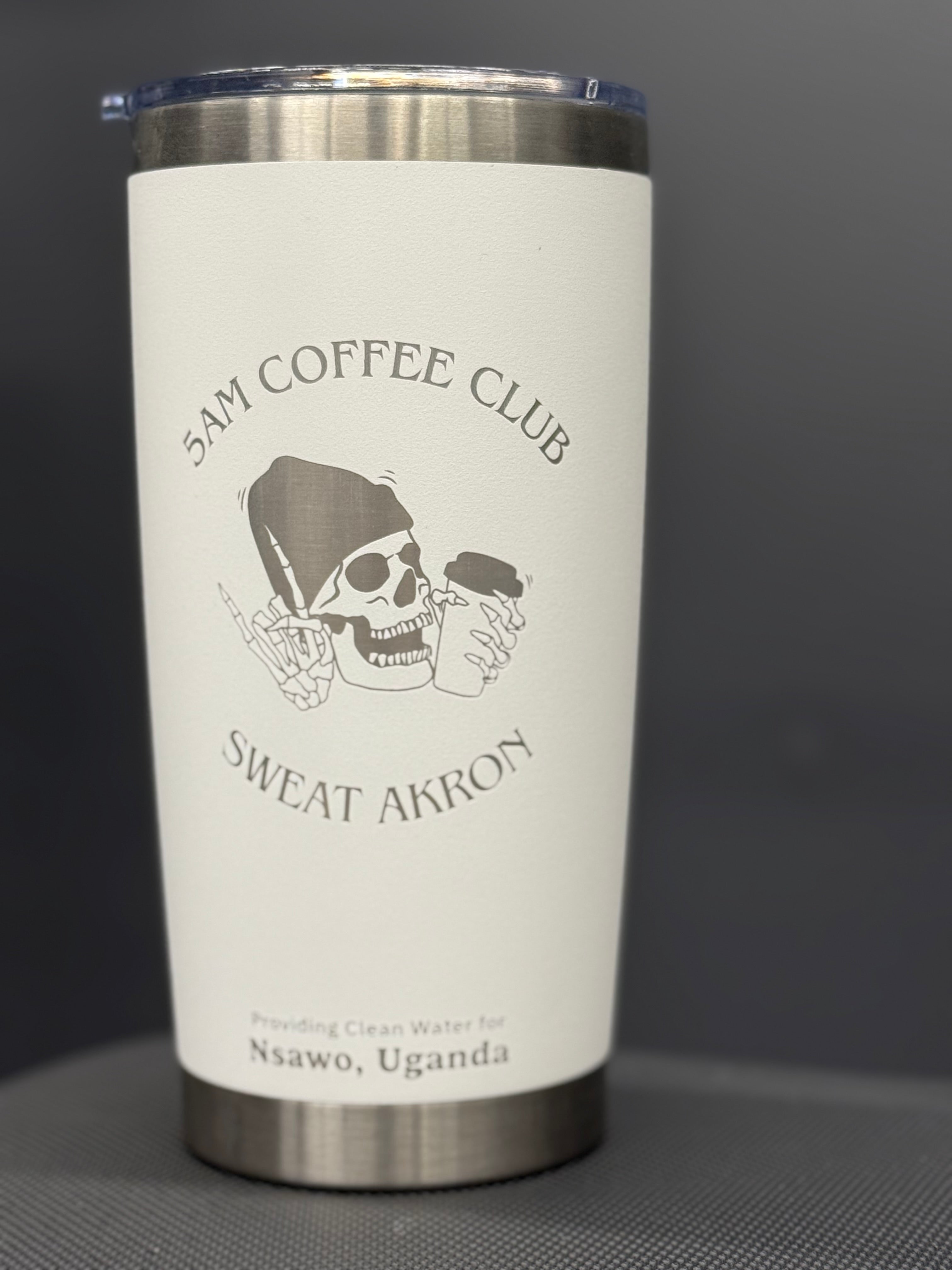 Stainless steel tumbler featuring "5AM Coffee Club" and "Sweat Akron" text with a skull graphic, promoting clean water for Nsawo, Uganda.